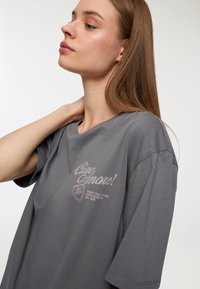 Szara bawełniana koszulka z okrągłym dekoltem i krótkimi rękawami. Na froncie znajduje się grafika serca oraz tekst w jasnych kolorach. Minimalistyczny design.