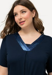 T-shirt navy con scollatura a V e rifiniture in satin a contrasto. Maniche corte, texture morbida e vestibilità rilassata.