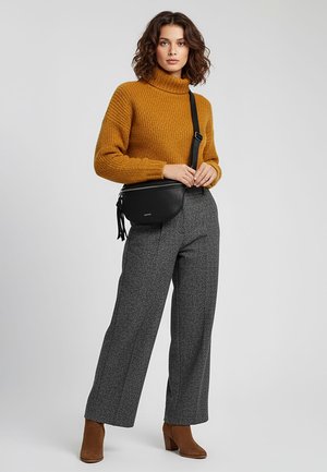 Mosterdgele gebreide coltrui, grijze geruite wijde broek, en bruine enkellaarzen; draagt een zwarte leren crossbodytas met franjes.