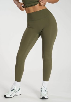 Mallas verde olivo con una cintura alta, textura suave, costuras planas y un diseño ajustado, combinadas con calcetines y zapatos deportivos blancos.