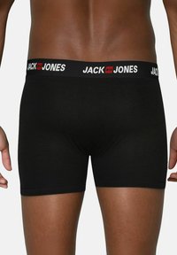 Zwarte boxershorts met een brede elastische tailleband waarop "JACK & JONES" in witte letters staat, aansluitend ontwerp met een gladde textuur.