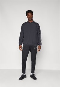 Sort atletisk træningsdragt med en langærmet top med rund hals og elastisk talje, parret med tapered bukser og sorte sneakers.