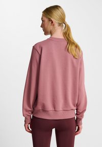 Lyserød sweatshirt med afslappet pasform, ribbede manchetter og kant. Glat bomuldsstof, vist fra ryggen med minimale detaljer synlige.