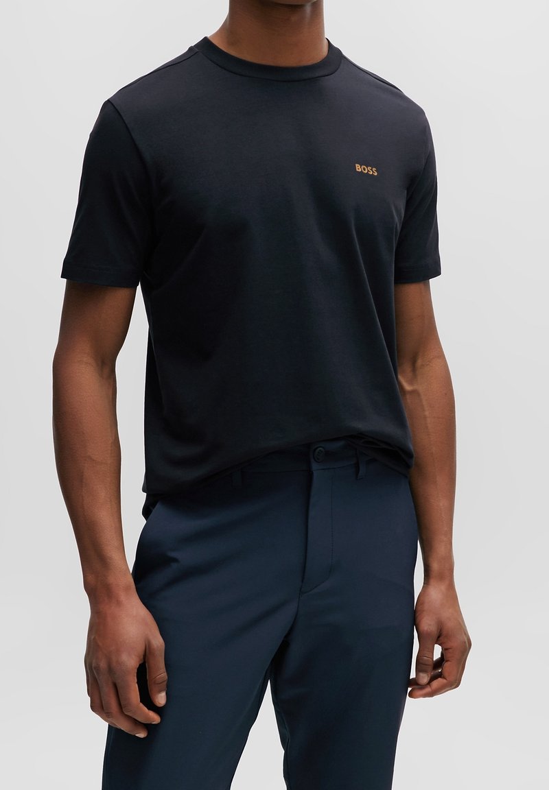 Černé bavlněné tričko s kulatým výstřihem, na hrudi s malým zlatým logem "BOSS". V kombinaci s námořnickými kalhotami.