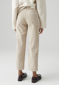 Pantaloni cropped in corduroy beige con due tasche posteriori e taglio dritto, abbinati a scarpe slip-on nere. Tessuto morbido e materiale resistente.