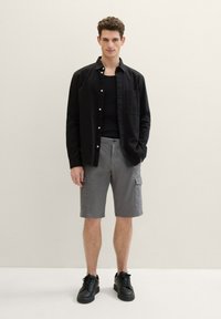Black button-up shirt over a black tank top, gray cargo shorts with side pockets, and black sneakers. Smooth fabric, casual fit.