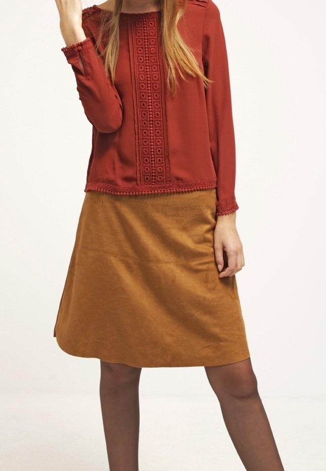 Haut à manches longues rouge avec des détails en dentelle, associé à une jupe en daim marron en forme de A. Le haut présente des accents texturés au niveau de l'encolure et des manches.