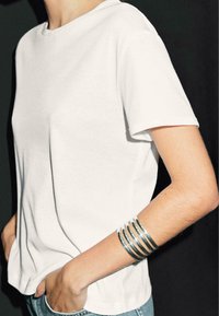 Hvid bomulds t-shirt med korte ærmer, parret med et sølv flerbånds armbånd. Blød tekstur, afslappet pasform og uformelt udseende.