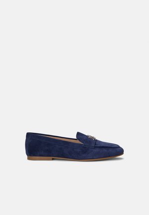 Donkerblauwe suède loafer met een platte bruine zool en zilveren decoratief metalen detail aan de bovenkant voor.