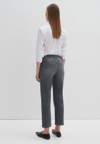 Jeans grises de talle alto con corte recto, de longitud ligeramente recortada y dos bolsillos traseros, combinados con una camisa blanca de botones.