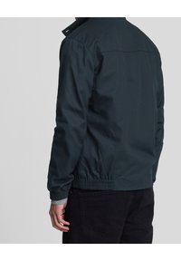 Dark green jacket made of a smooth, lightweight material. Features a stand collar, elastic waistband, and ribbed cuffs.