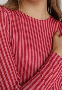 Haut à manches longues rayé rouge et rose avec une texture scintillante ; encolure ronde ; manches ajustées ; matière douce et extensible.