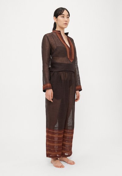 Pruun läbipaistev riidest rõivakomplekt sügava V-kaelusega, millel on kontrastsed oranžid triibulised aktsendid varrukate ja pükste alaosas.