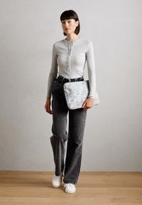 Grå ribbet langærmet top, sort bælte, mørke jeans, hvide sneakers. Holder en lyseblå taske med blomsterprint i rektangulær form.
