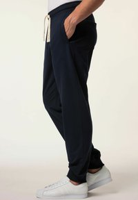 Navy Jogginghosen aus weichem Stoff mit elastischem Bund und Kordelzug sowie Seitentaschen. Kombiniert mit weißen Sneakers.