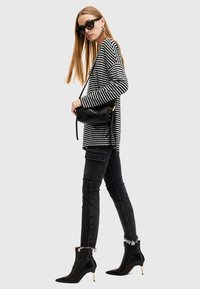 Maglione a righe bianche e nere, jeans neri con tasca a giorno, stivaletti neri con dettagli dorati e una piccola borsa nera.