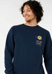 Navy blue long-sleeve sweatshirt made of cotton, featuring a logo with palm trees and sun in yellow and blue on the chest.