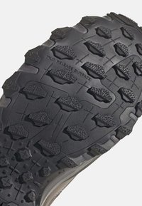 Semelle de chaussure en caoutchouc noir présentant de profonds motifs et une surface texturée avec "SURFACE ANTI-BAGAGE" en relief. Conçue pour l'adhérence et la durabilité.