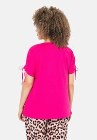 Fuchsiové bavlněné tričko s krátkým rukávem, se šňůrkami na manžetách pro úpravu. Nosené s kalhotami s leopardím potiskem.