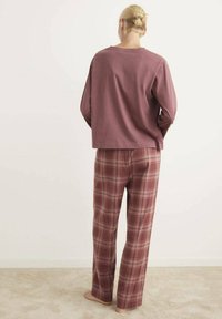 Mauve košeľa s dlhým rukávom skombinovaná s kockovanými nohavicami v odtieňoch burgundy a béžovej. Jemná tkanina, voľný strih a široké nohavice.