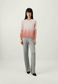 Suéter de gradiente rosa claro con un logo blanco, combinado con pantalones acanalados grises. El conjunto cuenta con mangas largas y pantalones ajustados hasta el tobillo.