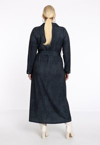 Robe chemise longue en denim foncé avec une taille ceinturée, des poignets boutonnés et un col. Texture lisse avec un subtil motif vertical.
