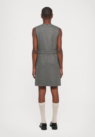 Graues ärmelloses Kleid mit strukturiertem Gewebe, das eine taillierte Taille und einen geraden Schnitt aufweist. Kombiniert mit knielangen Socken und schwarzen Schuhen.