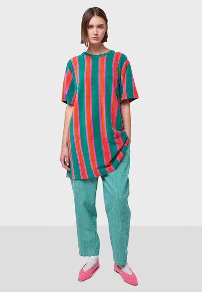 Prevelika zelena košulja s vertikalnim ružičastim i narančastim prugama, u kombinaciji sa svijetlozelenim hlačama s vertikalnim prugama i ružičastim balerinama.