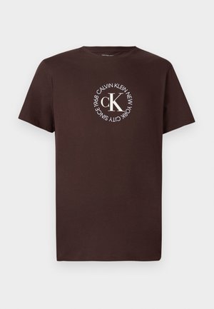 T-shirt marrone in cotone con maniche corte, con un logo circolare bianco con la scritta "CALVIN KLEIN NEW YORK SINCE 1968" e "cK" al centro.