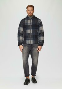 Kariertes Jackett in Grau und Marineblau mit einem Reißverschluss und einem Kragen, kombiniert mit grauen Jeans und schwarzen Sneakers. Glatte Textiloberfläche.