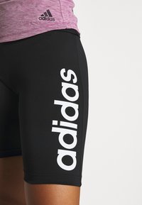 Czarne spodenki sportowe z dużym, białym brandingiem "adidas" z boku. Wykonane z lekkiego materiału o gładkiej teksturze.