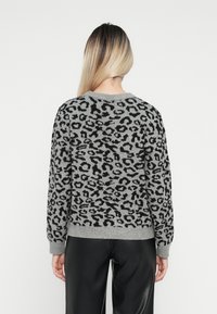 Un pull gris avec un motif léopard noir, tricot texturé, poignets et ourlet côtelés, avec un col rond classique. Porter avec un pantalon noir.
