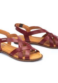 Rode leren sandalen met kruisbanden en een verstelbare enkelriem. Bruine leren binnenzool, platte rubberen buitenzool en geweven ontwerpdetails.