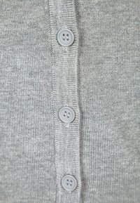 Grå stickad cardigan med fem grå knappar framtill, med en mjuk textur och en enkel, okomplicerad design.