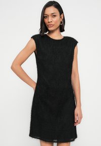 Μαύρο αμάνικο φόρεμα με απαλή, υφή υφάσματος· άνετη εφαρμογή· μήκος έως το γόνατο· στρογγυλεμένος λαιμός· μίνιμαλ σχεδιασμός χωρίς ορατά κλειδώματα.