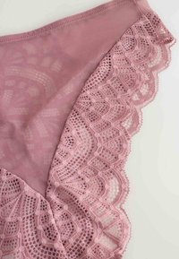 Helle rosa Slips aus weichem Stoff, mit gewelltem Spitzenrand und geometrischem Muster entlang der Kanten.