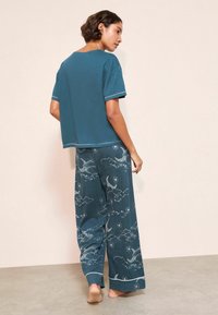 Tirkīza krāsas brīvdienu apģērbu komplekts, kas sastāv no kvadrātveida, īsām piedurknēm t-krekla un plašām biksēm ar mākoņu un mēness rakstu. Mīksts audums ar kontrastējošiem šuvēm.