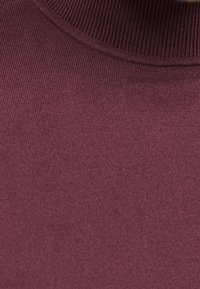 Nahaufnahme eines bordeauxfarbenen gerippten Strickrollkragenpullis, der die Textur des Stoffes und die Detailansicht des Kragens zeigt.