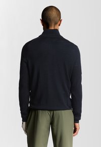Maglione blu navy a maglia con colletto alto, polsini a coste e texture liscia. Presenta una silhouette aderente e dettagli delle cuciture sottili.