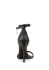 Zwarte hoge hak sandaal van soepel leer, met een dunne enkelband met gouden hardware en een slank puntige teen ontwerp.