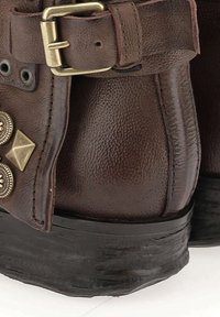 Brązowe skórzane botki za kostkę o teksturowanym wykończeniu, z klamrą i dekoracyjnymi złotymi akcentami, w tym ćwiekami i nitami.