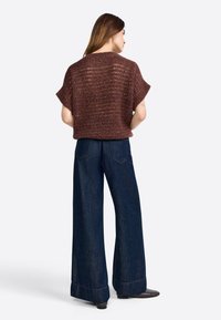 Brauner gestrickter, kurzärmeliger Cropped-Pullover, kombiniert mit weit geschnittenen, dunkelblauen Jeans, präsentiert aus einer Rückansicht mit glatter Textur.
