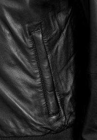 Zwarte leren jas close-up die een gladde textuur toont, een zijzak met klep en elastische manchetten aan de onderkant.