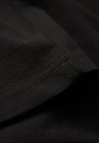 Tela de algodón negra que muestra una vista en primer plano de la textura suave, tejido fino y costura ordenada a lo largo del borde.