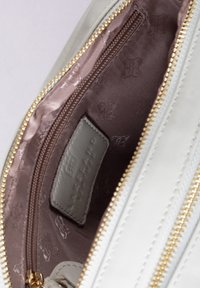 White leather pouch with gold zipper. Interior features light brown lining with subtle pattern. Includes a fabric label inside.