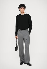 Black sweater, gray pinstriped pants, black shoes, holding a small black bag. Smooth texture, fitted design, and tailored look.