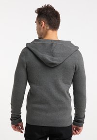 Grijze hooded sweater van een gestructureerde brei. Heeft lange mouwen met geribbelde manchetten en een relaxte pasvorm. De achteraanzicht toont het ontwerp van de capuchon.