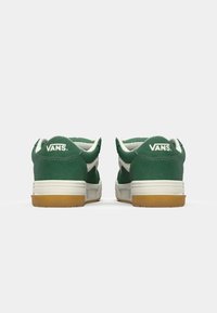 Zelené semišové tenisky s bielymi akcentmi. Majú biely bočný pás, polstrovaný golier a gumovú podrážku. Na päte je značka "VANS".
