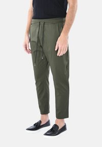 Pantaloni a sigaretta verde oliva con vita elastica e coulisse nera, abbinati a scarpe slip-on nere con suola bianca.