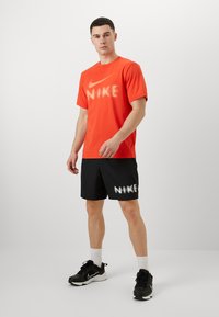 Punane Nike T-särk suure valge logo ja mustade lühikeste pükstega, millel on sarnane logo. Mustad sportlikud kingad ja valged sokid lõpetavad riietuse.